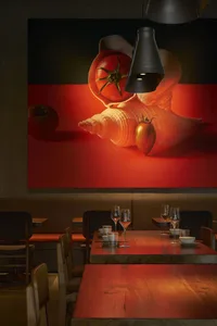 現代餐廳室內擺放木製餐桌，搭配紅色燈光與大型蕃茄壁畫