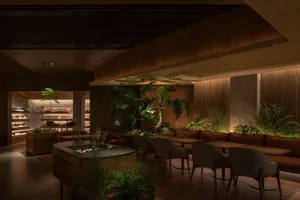 A modern restaurant interior featuring wood, concrete walls, plants, and dark lighting.