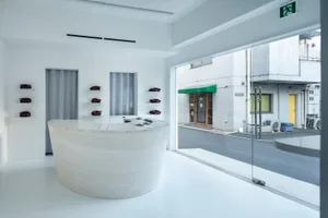 A minimalist retail storefront with a large, curved white marble reception desk and purple bags displayed on shelves against 