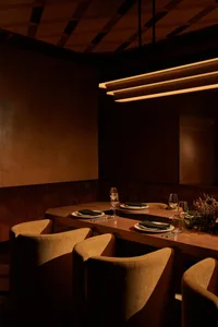 A modern restaurant dining room with wood furniture and a long table set for four.