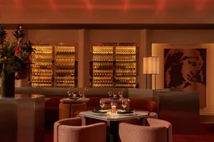 A warmly lit restaurant interior with a wine bar featuring modern furniture and a variety of bottles on display.