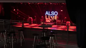 An empty industrial-style event space with red and black lighting and stage setup.