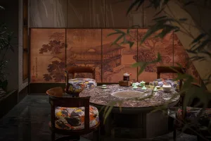 A modern tea room with a round marble table and chairs with patterned cushions, surrounded by traditional Chinese artwork.