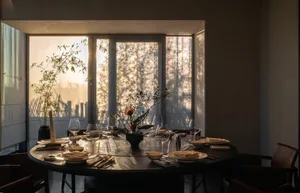 A modern dining room setting with round table, chairs, and decorative elements under bronze lighting.