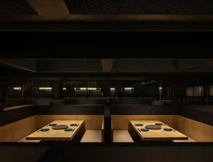 An elegant, minimalist restaurant interior with wooden tables and seating areas.