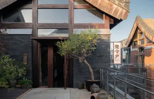 Modern restaurant exterior with brick and concrete materials, featuring black bricks and a potted tree.