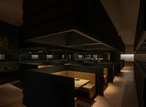Modern restaurant interior with wooden tables and chairs, concrete walls, and warm lighting.