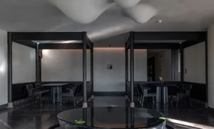 A dark, modern restaurant interior with black marble countertops, black walnut seating, and concrete framing.