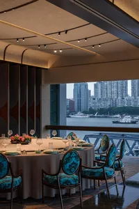 A modern restaurant interior with teal upholstered chairs, round tables, and a view of the cityscape.