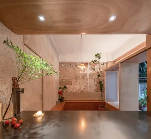 A modern living room with exposed concrete walls and a polished concrete floor, featuring green plants and a minimalist desig