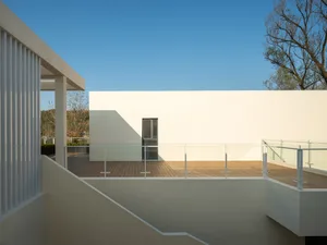 A minimalist modern rooftop deck with wooden flooring and white walls, under a clear blue sky.