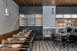 Industrial restaurant dining area with wooden furniture, metal counter, and black and white floor pattern