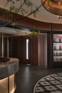 A modern coffee shop reception area with a wooden counter, marble floor, and glass display case.