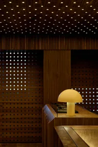 A modern interior with a wooden retail shopfront featuring a table lamp and a perforated wood wall.