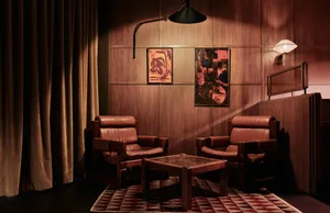 An industrial-style living room features comfortable brown leather armchairs and a wooden table