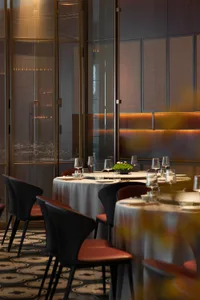 A modern restaurant interior featuring dark wood, glass, and marble materials, with tables set for dining.