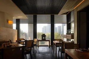 Modern restaurant dining area with concrete walls, wooden tables, and black wooden blinds.