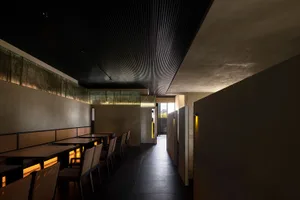 Modern restaurant interior with wooden tables, concrete walls, and warm lighting.