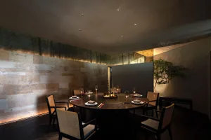 Modern restaurant interior with wood and marble materials, featuring a round dining table with place settings and wine glasse