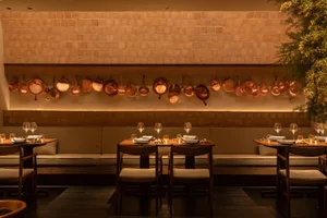 Restaurant interior with brick walls and wooden seating areas, featuring hanging copper pots and glasses on tables.
