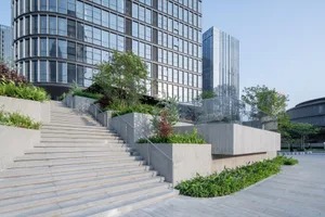 Modern public space facade featuring concrete stairs, glass skyscrapers, and greenery.