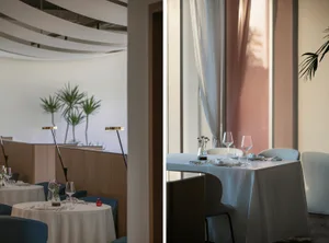 Tables set in a minimalist restaurant interior with white walls and curtains, featuring geometric ceiling design.