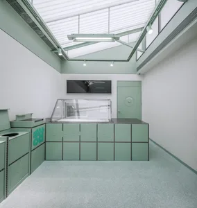 A modern cafe interior with a green panel-covered counter, glass display case, and minimalist design.