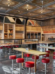 Industrial-style restaurant interior with metal, glass, and wood elements, and red leather stools.