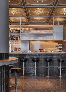 Modern restaurant bar counter featuring a terrazzo floor, glass shelves, and metallic bar stools.