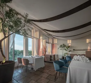 A modern restaurant interior with large windows, elegant seating, and greenery.