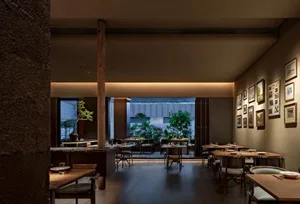 A modern restaurant interior featuring wooden tables, stone details, and green plants.