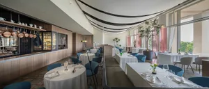 Modern, brightly-lit restaurant interior with white tables and blue chairs.