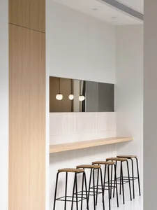 A minimalist bar counter with wooden seats and pendant lights.
