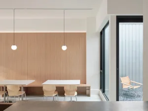 Contemporary office space featuring minimalist design with wooden furniture, concrete flooring, and glass partitions.