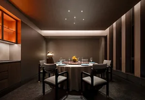 A modern, minimalist dining room with moody lighting and a round table surrounded by six chairs.