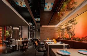 A modern restaurant interior with sleek concrete flooring, metal accents, and glass walls.