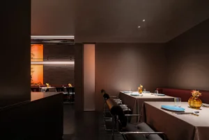 A modern restaurant interior with textured materials, featuring tables, chairs, and decorative elements.