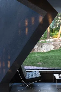 Black leather chair with metal legs in front of a window overlooking a garden with rocks and grass.