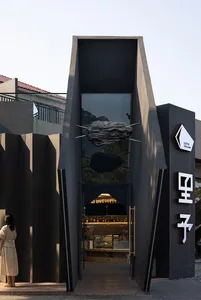 A modern storefront with black metal and glass elements, featuring a metallic cloud sculpture.