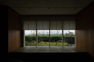 A modern living room features large windows overlooking a tranquil garden with plants, rocks, and a city skyline.