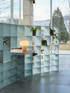 A minimalist living room with a glass partition, green plants, and a glowing table lamp.