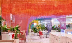 A contemporary restaurant interior featuring orange drapery and various plants and furniture.
