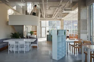 A modern cafe interior with concrete walls and a mix of furniture styles, including a round balcony with a white railing and 