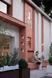 A modern storefront with concrete walls and green plants in planters.