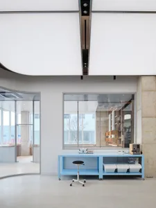 A modern, minimalist workstation with a blue table and a black stool in an open office space.