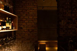 An industrial-style wine bar featuring exposed brick walls and a variety of wine bottles and glasses on shelves and tables.