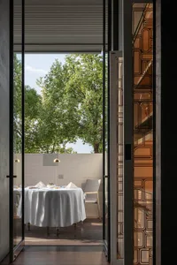 A modern restaurant interior with glass walls and wooden flooring, featuring a round table set for a meal.