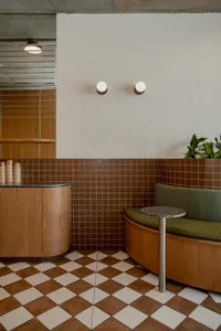 A modern cafe interior with a wooden floor, tiled walls, and green cushioned seating.