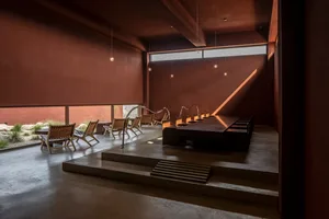 Modern restaurant interior with concrete floors, minimalist furniture, and a large window allowing natural light to enter.