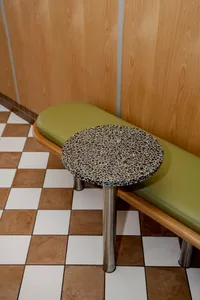 A modern restaurant interior with a round, speckled black countertop on a checkered tile floor.